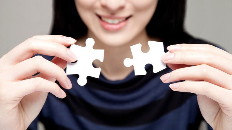 smiling woman holding puzzle pieces that fit together